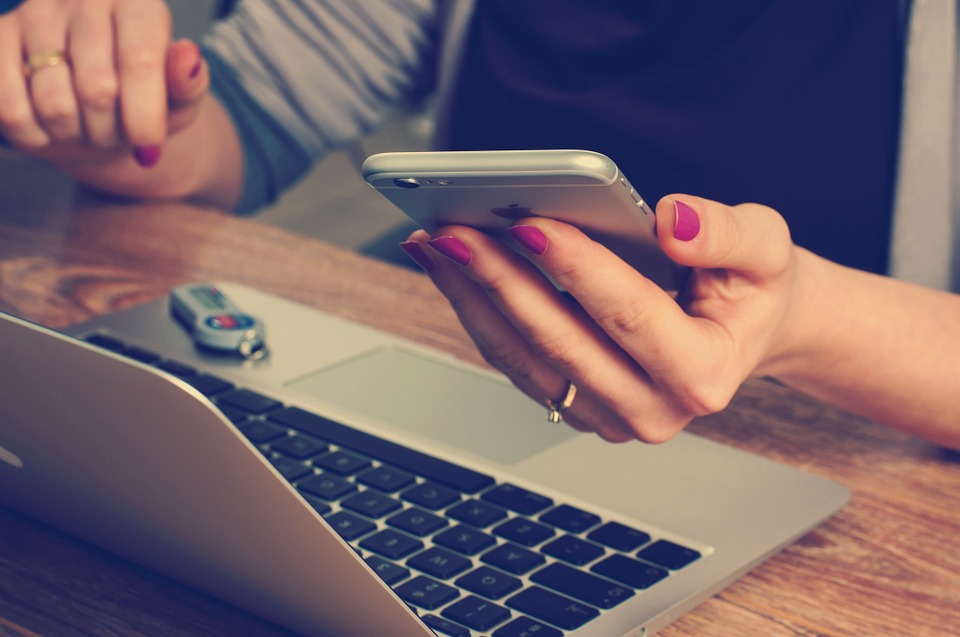 Woman Browsing on Mobile Phone in Front of a Laptop